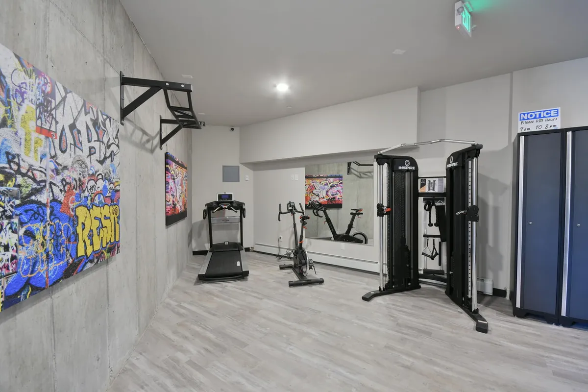 A modern, well-equipped gym featuring a treadmill, stationary bike, weight machine, and vibrant graffiti art on the walls. The space is bright, motivating, and designed for both personal and group workouts.