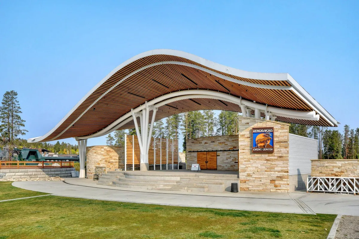 An exterior shot of a community event center, marked by a striking curved roof, stone facade, and wooden accents. The setting is lively and festive, suggesting opportunities for gatherings, performances, and local events.