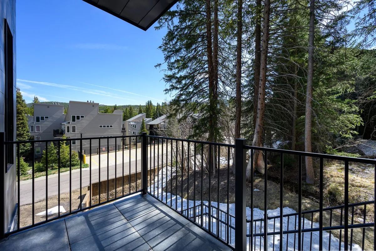 A peaceful balcony space with a sturdy railing, surrounded by tall trees and a clear view of neighboring buildings. The ambiance suggests a quiet spot for enjoying sunrise coffee or evening stargazing, emphasizing seclusion and nature immersion.