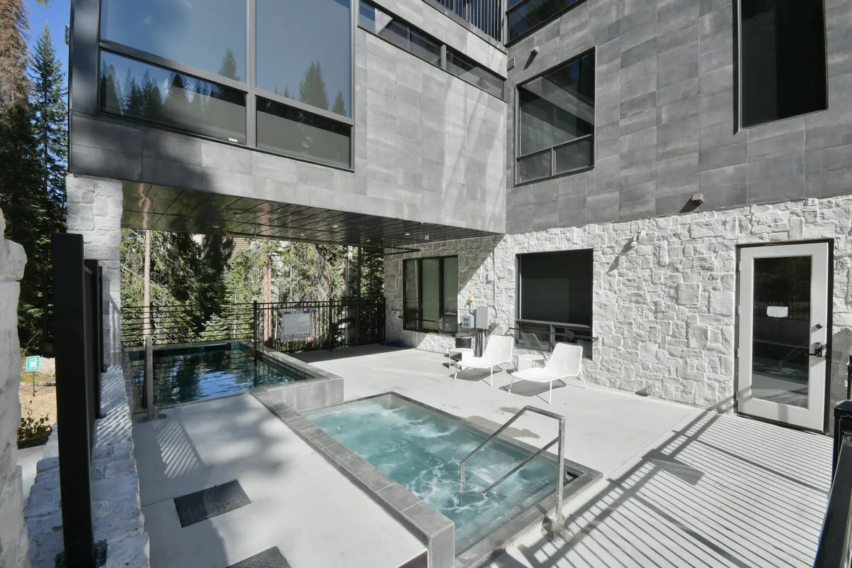 An inviting view of an oversized outdoor hot tub and swimming pool set against a backdrop of lush landscaping and striking architectural design. Comfortable outdoor seating surrounds the area, perfect for relaxing after a day on the trails or slopes.