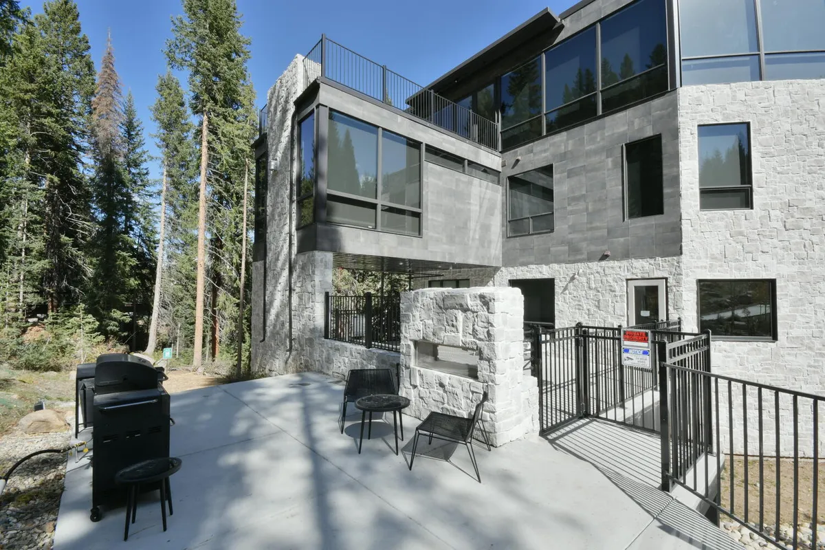 A modern, inviting patio space with contemporary outdoor seating, a grill for alfresco dining, and large windows connecting the patio to the home's interior. The scene is surrounded by tranquil forest views, capturing the feeling of privacy and immersion in nature.