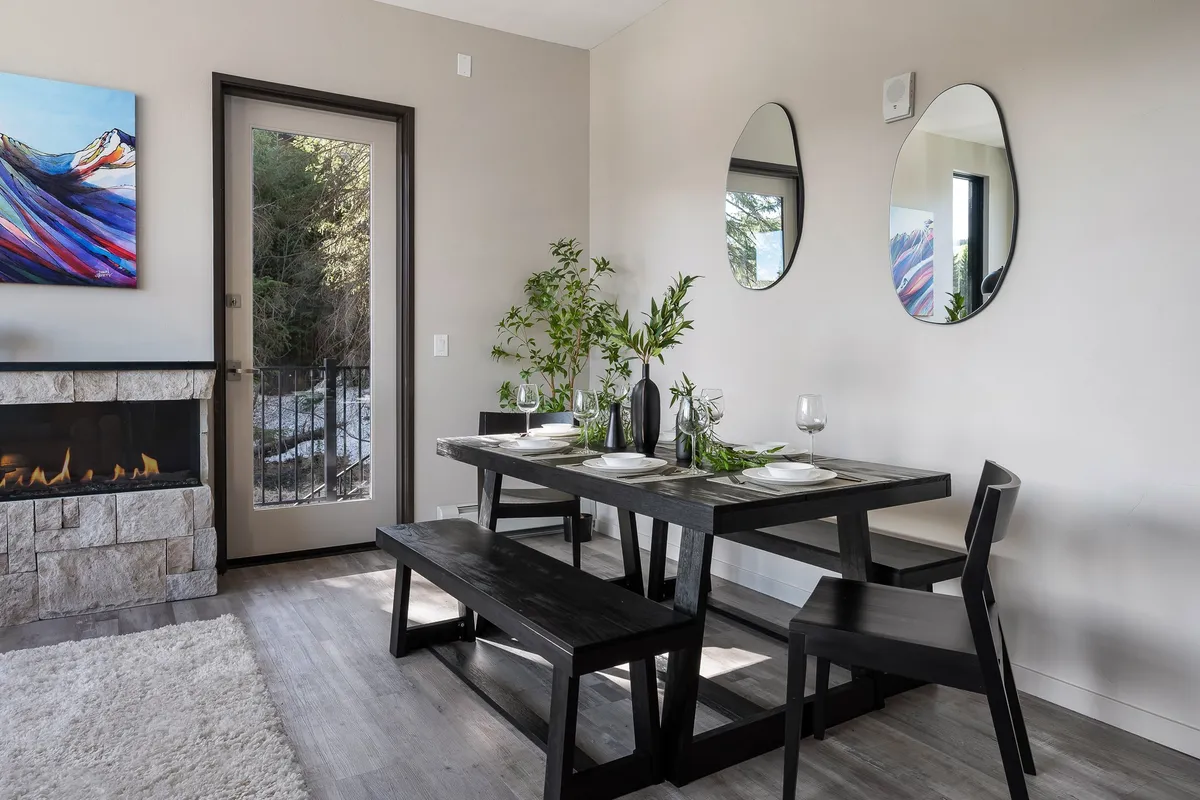 A stylish dining area set beside a fireplace, with a contemporary dining table, artwork on the wall, and mirrors adding depth. The setting suggests an inviting space for both quiet meals and special celebrations.