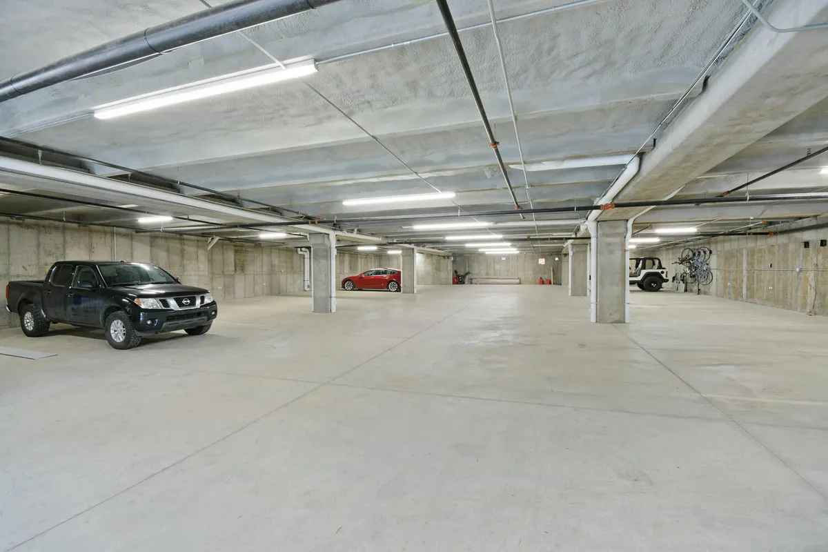 A spacious and well-lit underground parking garage with two vehicles parked between sturdy concrete pillars and overhead lighting, illustrating ease of access and secure parking.