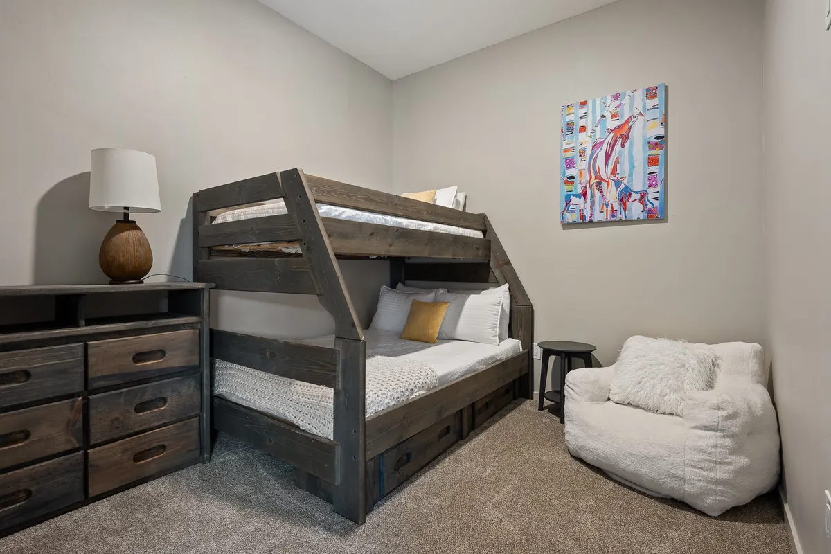 A family-friendly bedroom with a full-over-full bunk bed, playful artwork, a chest of drawers, and a bean bag chair. The arrangement suggests an inviting space for kids to relax, play, and sleep comfortably.