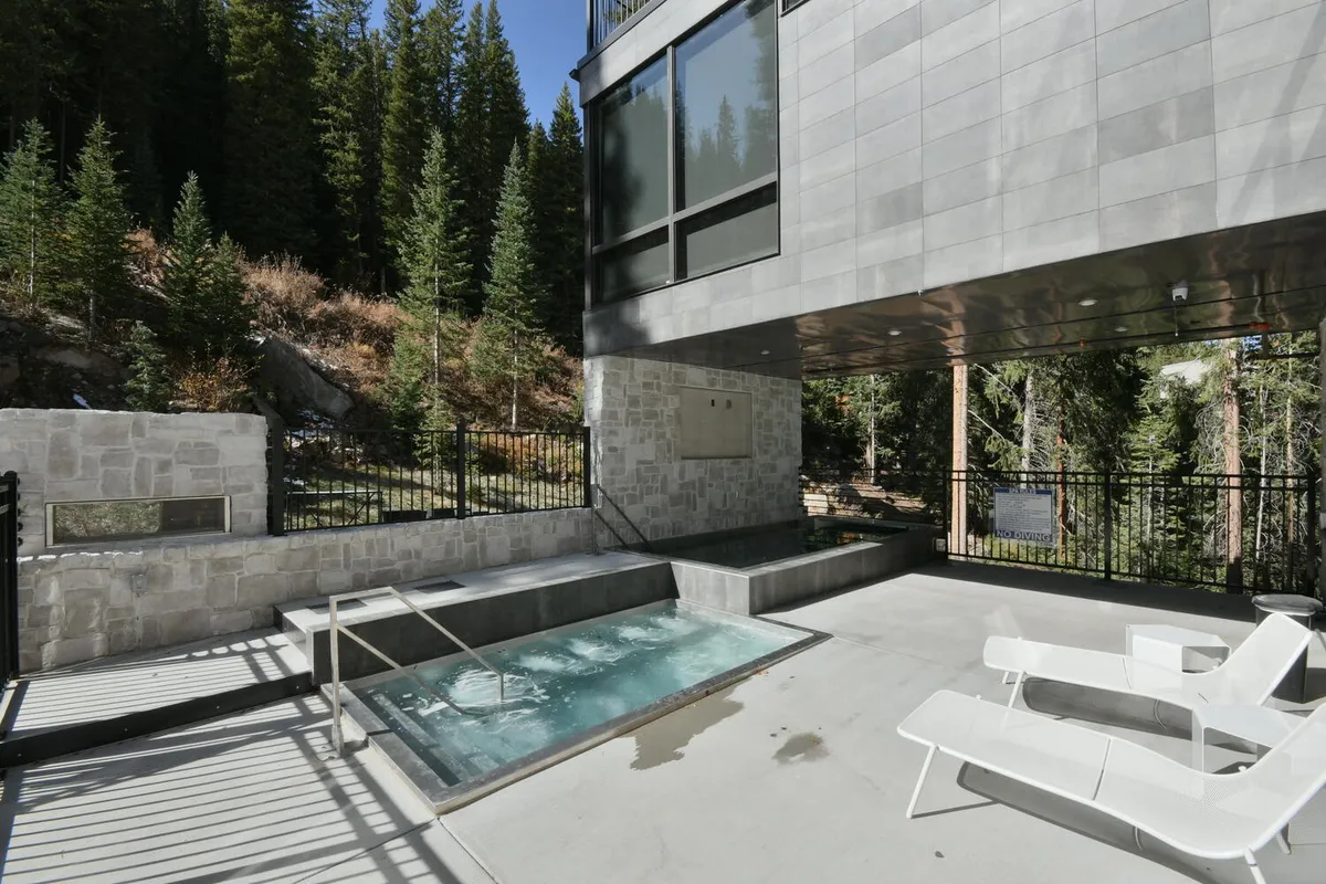 An inviting outdoor hot tub set against a forest backdrop, with lounge chairs and stone walls, suggesting relaxation after a day of adventure. The sun-dappled setting offers a tranquil counterpoint to high-energy activities.